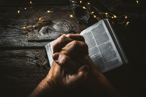 hands in prayer form over open bible on wooden table